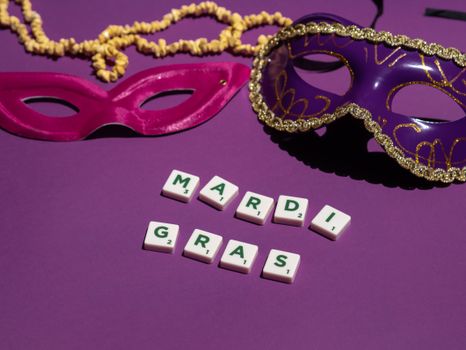 Vibrant Mardi Gras themed masks and letter tiles on a purple background.