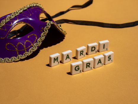 Vibrant purple Mardi Gras mask with letter tiles on a yellow background, celebrating a festive theme.
