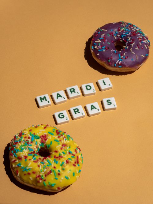 Free Two vibrant donuts with sprinkles and letter tiles spelling 'Mardi Gras' on an orange background. Stock Photo