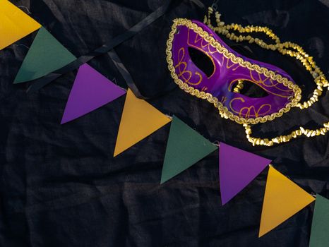 Colorful Mardi Gras mask and pennants on black fabric capturing festive spirit.