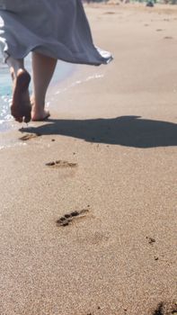 A person walks barefoot on a sandy beach, leaving footprints behind under the bright sunlight.