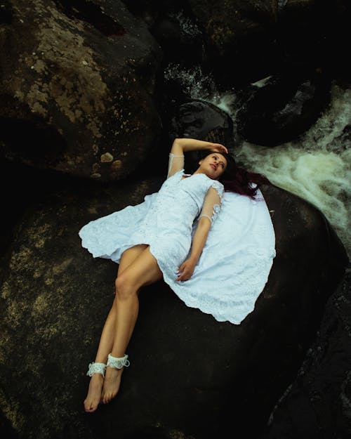 Free Woman in White Dress Lying on Big Rock Formation while Looking Afar Stock Photo