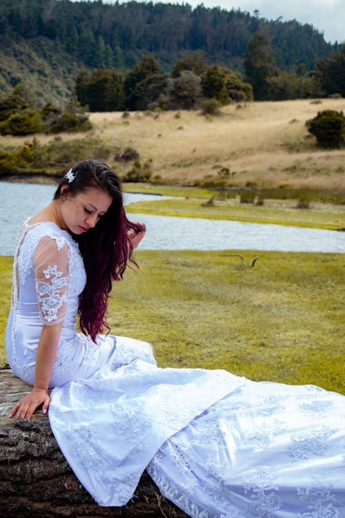 Woman in White Wedding Gown Sitting on Big Rock while Looking Down