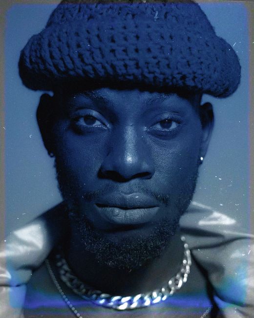 Fashionable black man wearing jewelry and knitted hat, looking at camera in unique blue tint.
