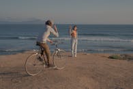 一对夫妇在海边互相挥手致意，一人在海滩上骑自行车