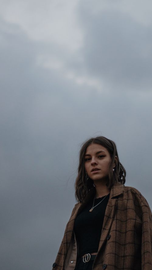 Free Capture of a woman in a plaid coat against a moody cloudy sky, exuding modern style. Stock Photo