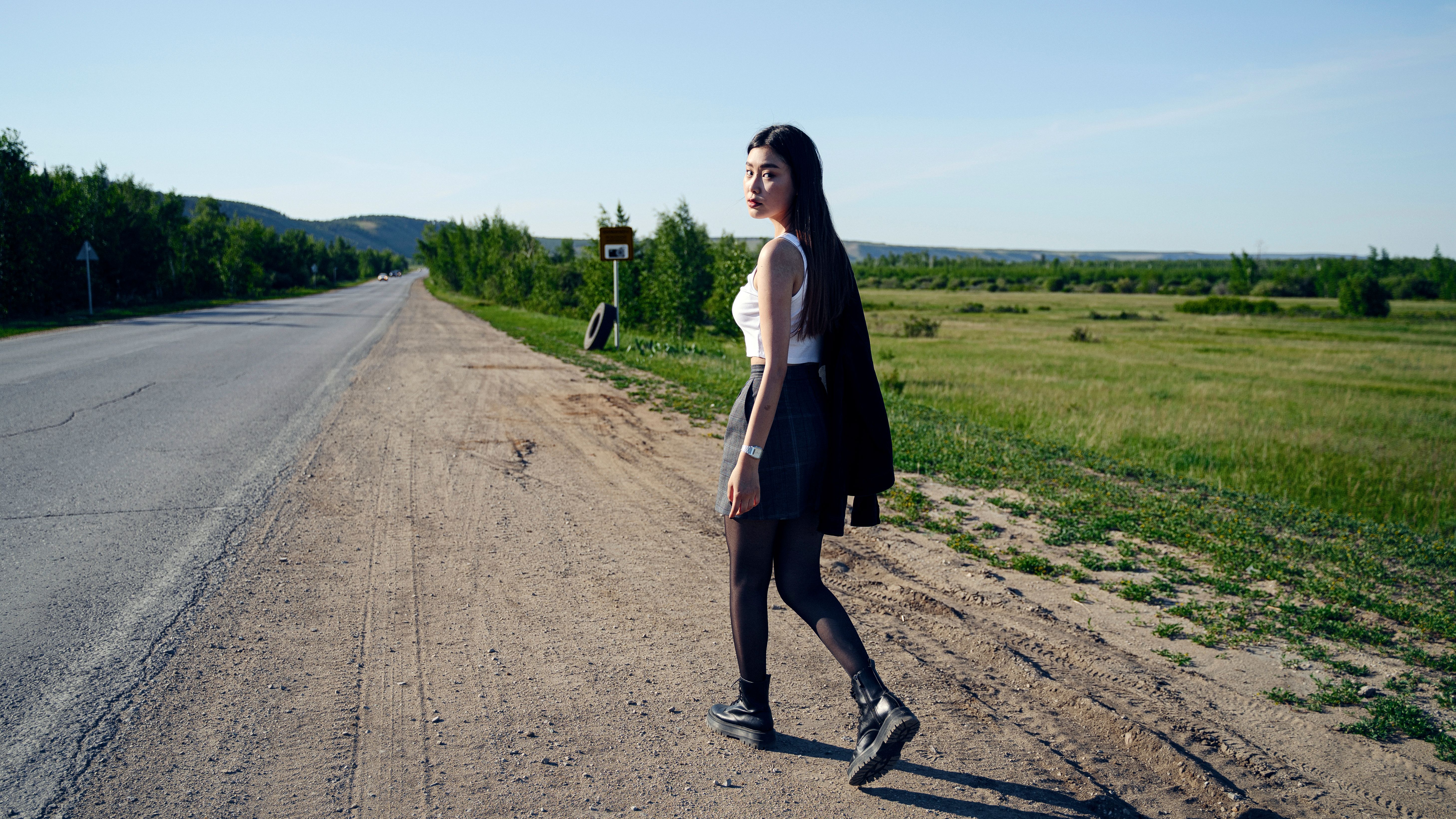 Young woman walking along a rural road in summer, showcasing travel and adventure.