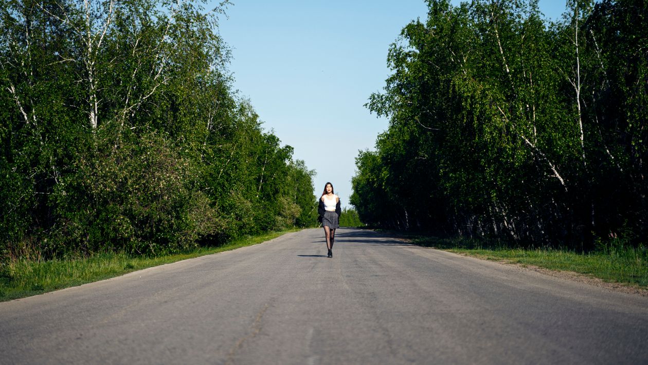 A Woman in White Tank Top Walking on the Road Between Green Trees ...
