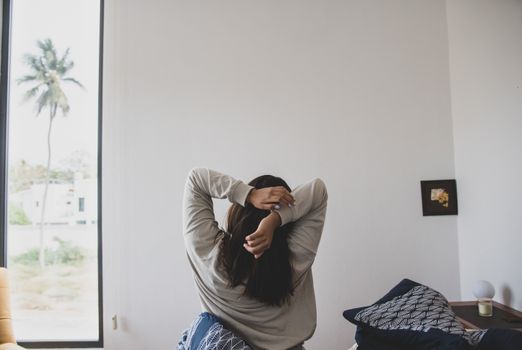 A woman stretching in a modern bedroom with morning light, offering a sense of relaxation and tranquility.