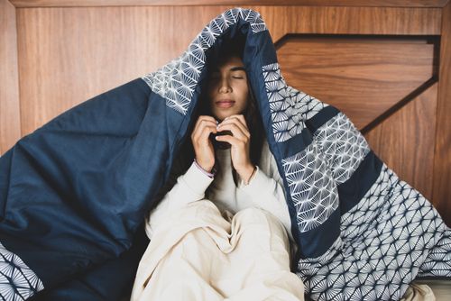 Free Woman wrapped in a blanket indoors, eyes closed, presenting a calm and cozy atmosphere. Stock Photo