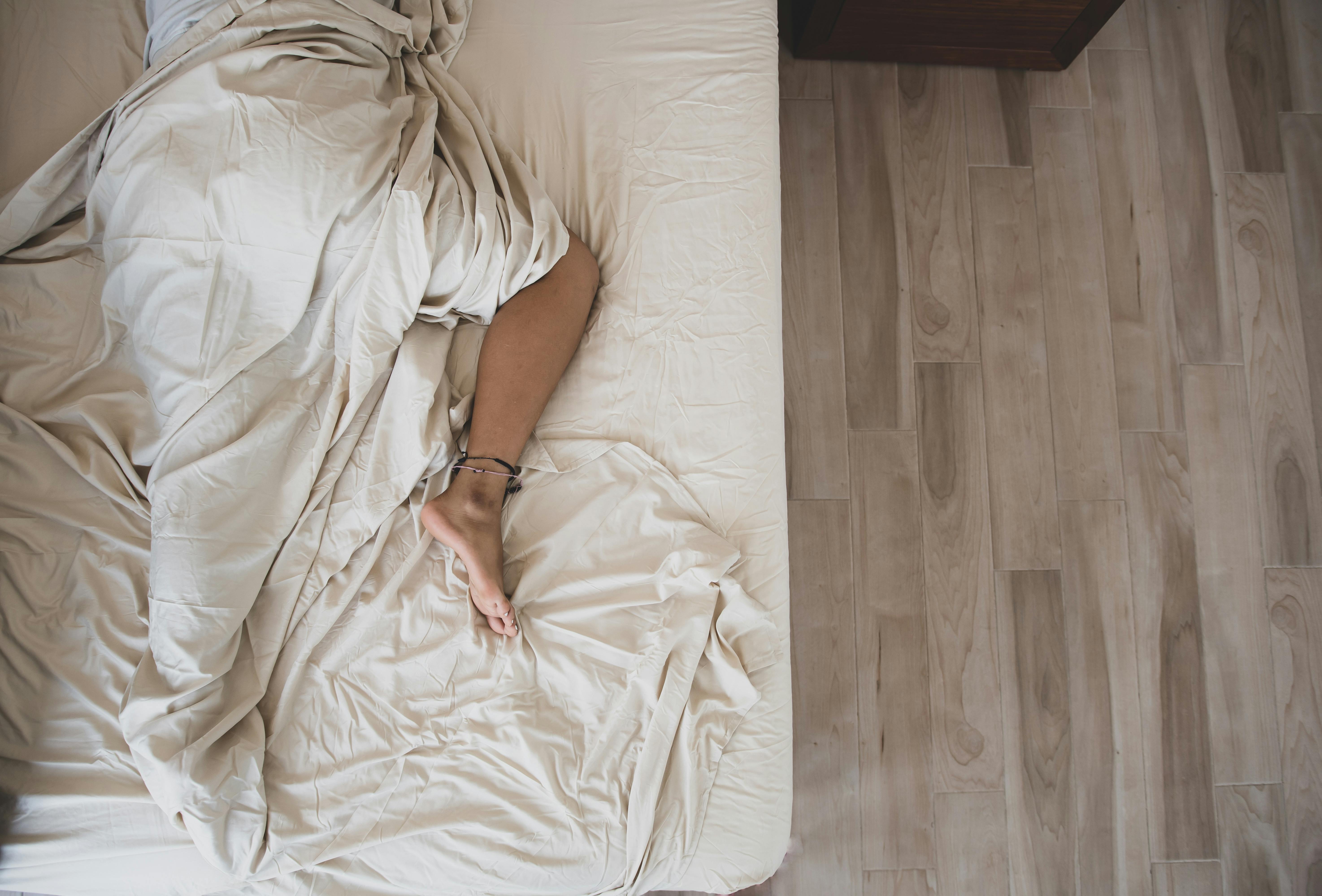 An adult sleeping under soft white sheets in a tranquil bedroom. Top view.