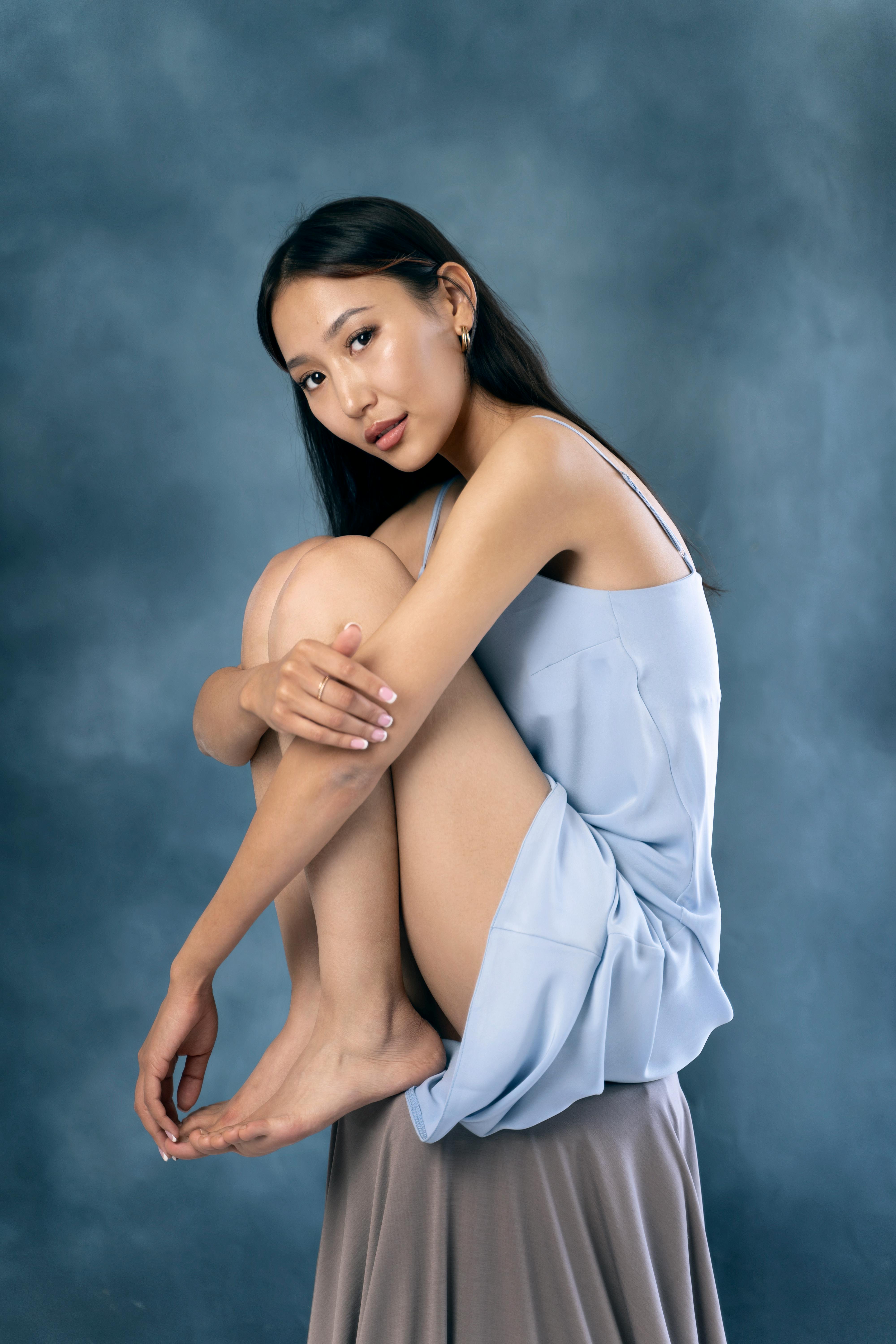Graceful woman seated in a studio setting, captured in a relaxed pose against a soft background.