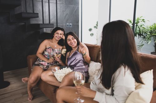 Free Three friends enjoy a relaxed indoor evening with wine and popcorn, sharing smiles and conversation. Stock Photo