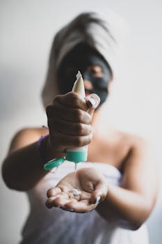 Close-up of a woman applying facial cream with a face mask and towel headwrap at home.
