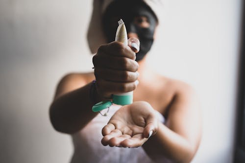 Woman in Beauty Mask Using Cream from Bottle