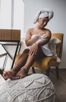 Woman in towel performs body care routine in a cozy indoor setting. Healthy lifestyle focus.
