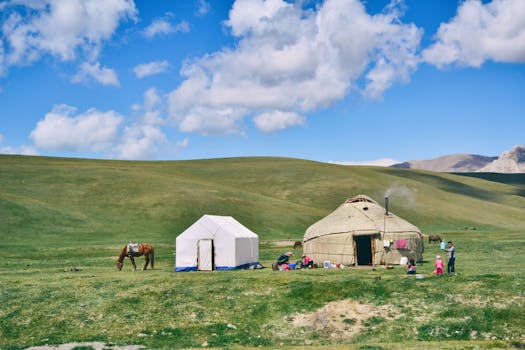Serene rural landscape with a yurt, tent, and grazing horse under a blue sky.
