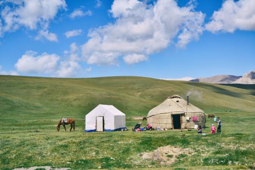 Free Serene rural landscape with a yurt, tent, and grazing horse under a blue sky. Stock Photo
