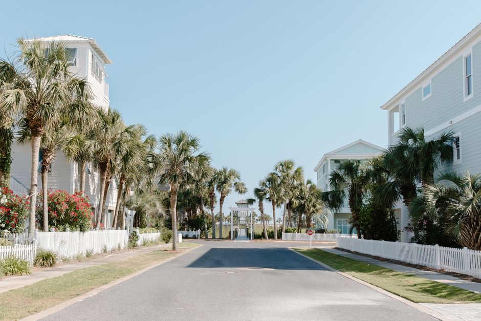 A peaceful coastal street lined with palm trees and charming houses under a clear sky.