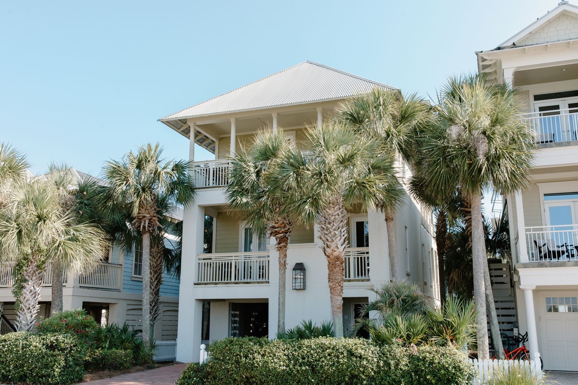 Sunny beach house exterior surrounded by lush palm trees and blue sky.