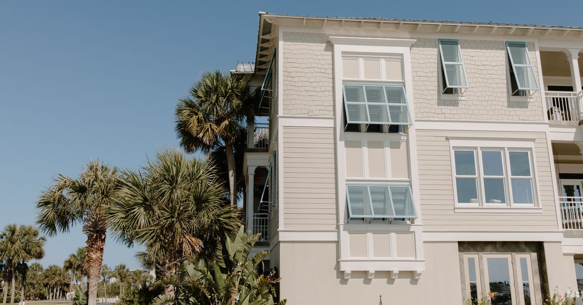 Stylish beach house facade with palm trees and blue sky backdrop.
