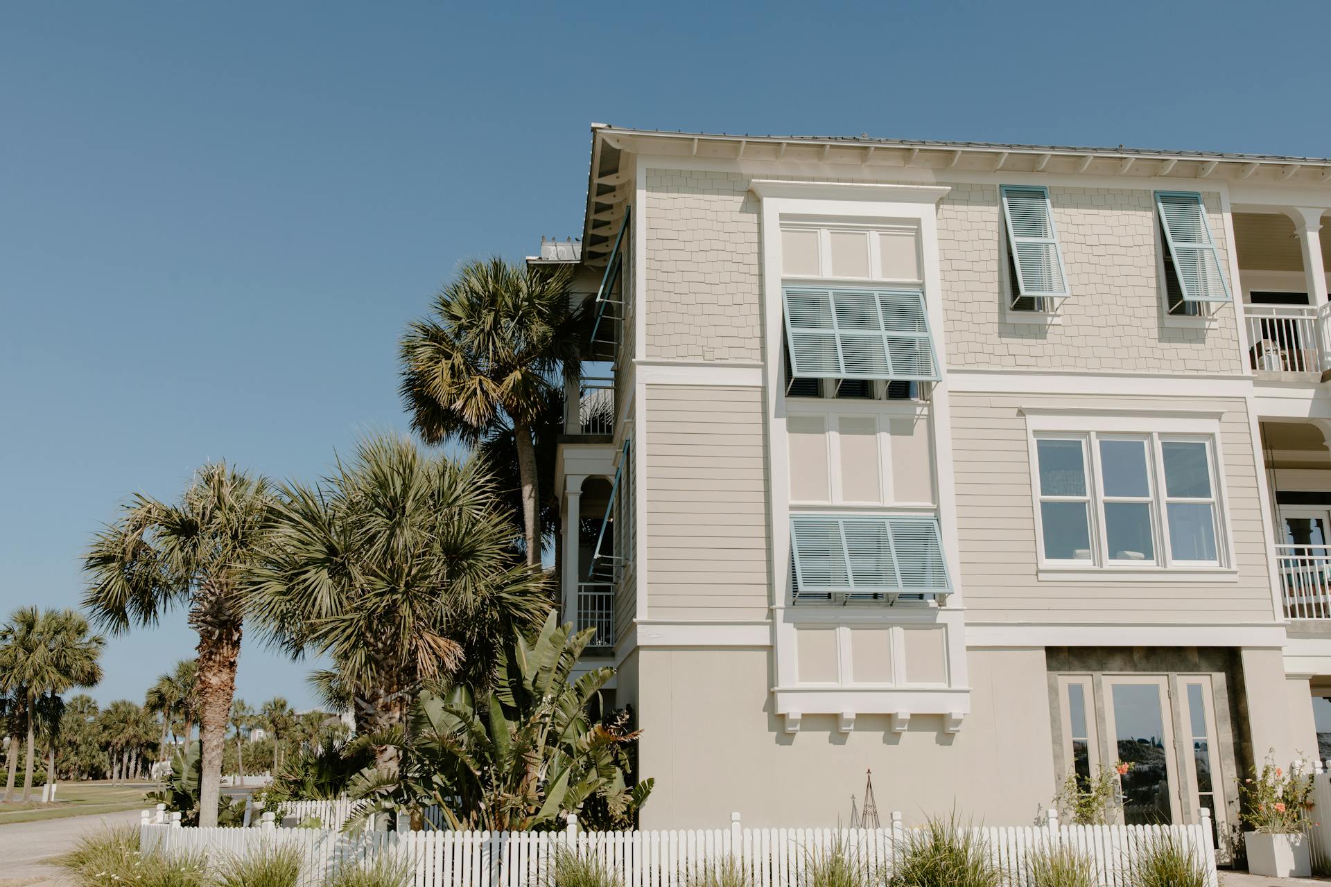 Stylish beach house facade with palm trees and blue sky backdrop.