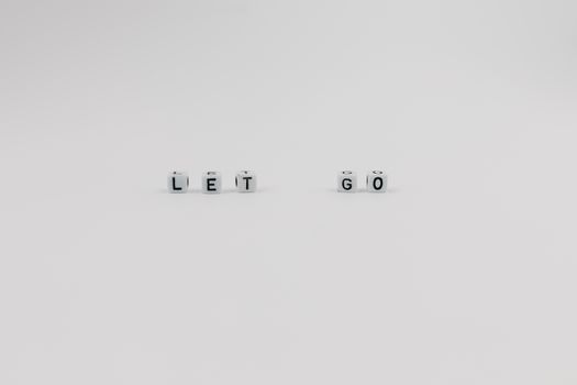 Simple white dice spelling 'LET GO' on a plain surface, conveying inspiration and motivation.
