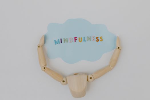 Wooden mannequin arms holding a blue cloud with 'Mindfulness' text, promoting self-awareness.