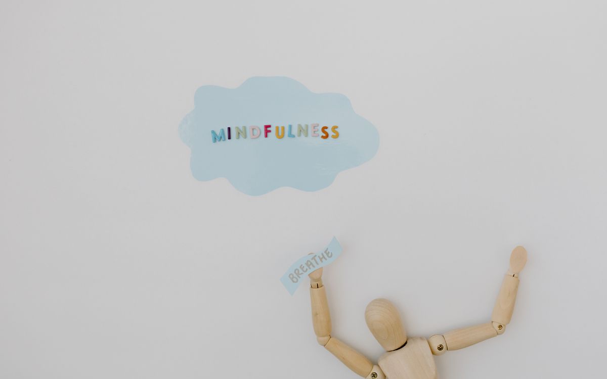 Wooden figure holding 'breathe' text with 'mindfulness' cloud on white background.