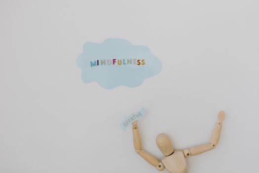 Wooden figure holding 'breathe' text with 'mindfulness' cloud on white background.