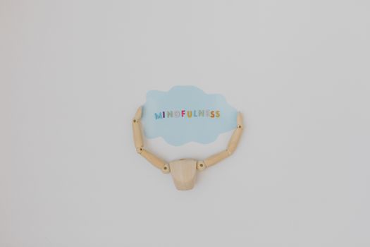 Minimalist image of a wooden figure holding a speech bubble saying 'Mindfulness'.