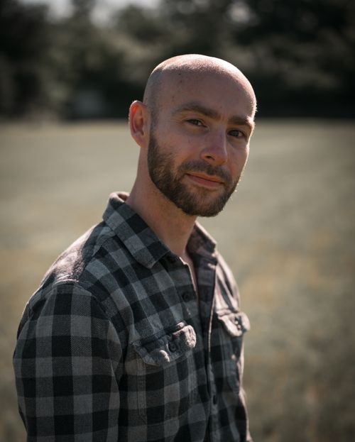 Free A bald man with a beard poses outdoors in a checkered shirt under natural light. Stock Photo