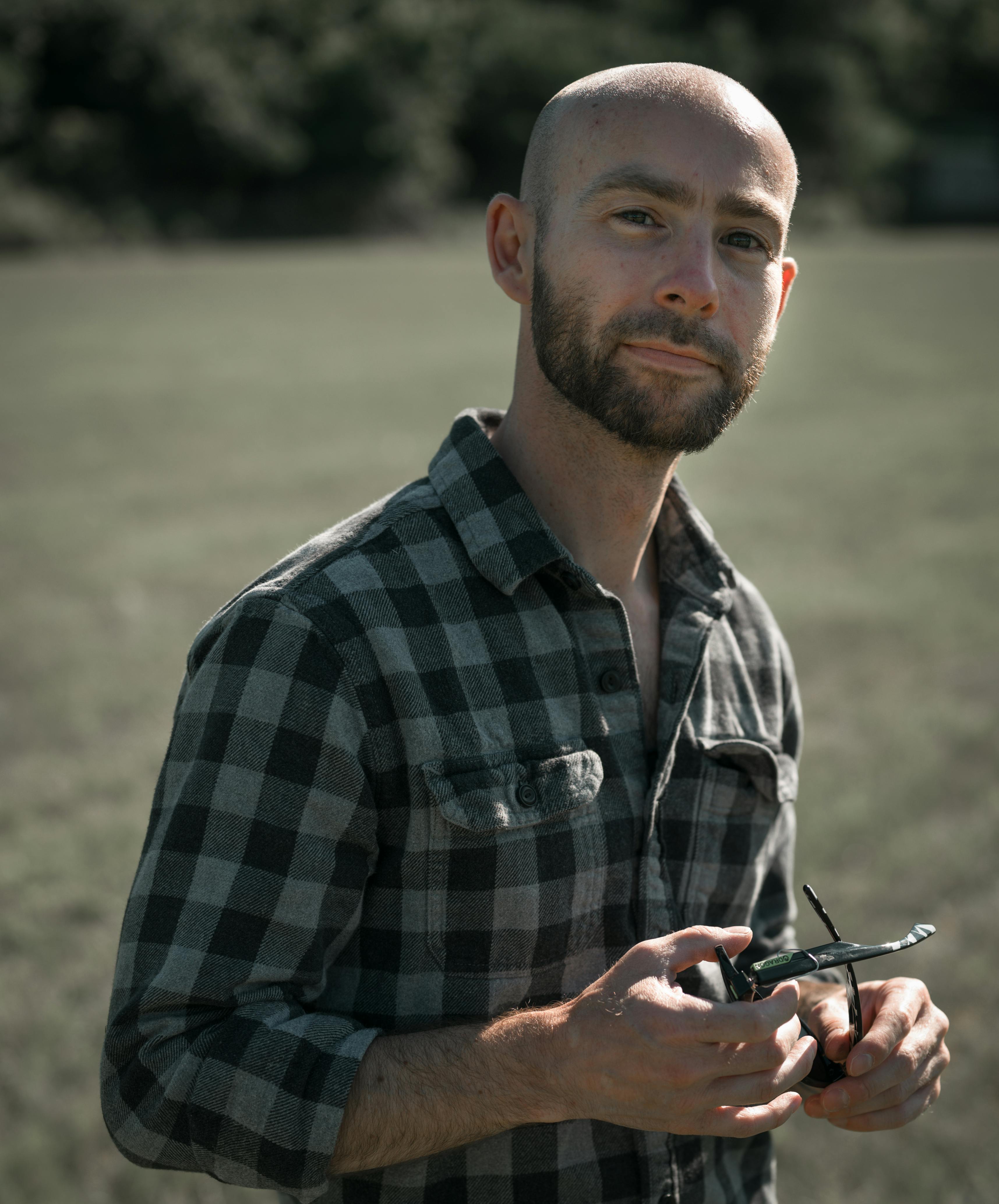 Portrait of a bald man with a beard holding sunglasses on a sunny day in nature.