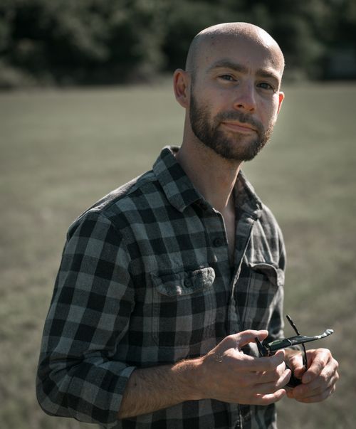 Free Portrait of a bald man with a beard holding sunglasses on a sunny day in nature. Stock Photo
