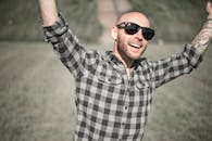 Selective Focus Photo of a Man with Sunglasses Raising His Hands