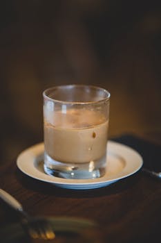 Refreshing iced latte in a glass with a saucer on a wooden table, perfect for café ambiance.