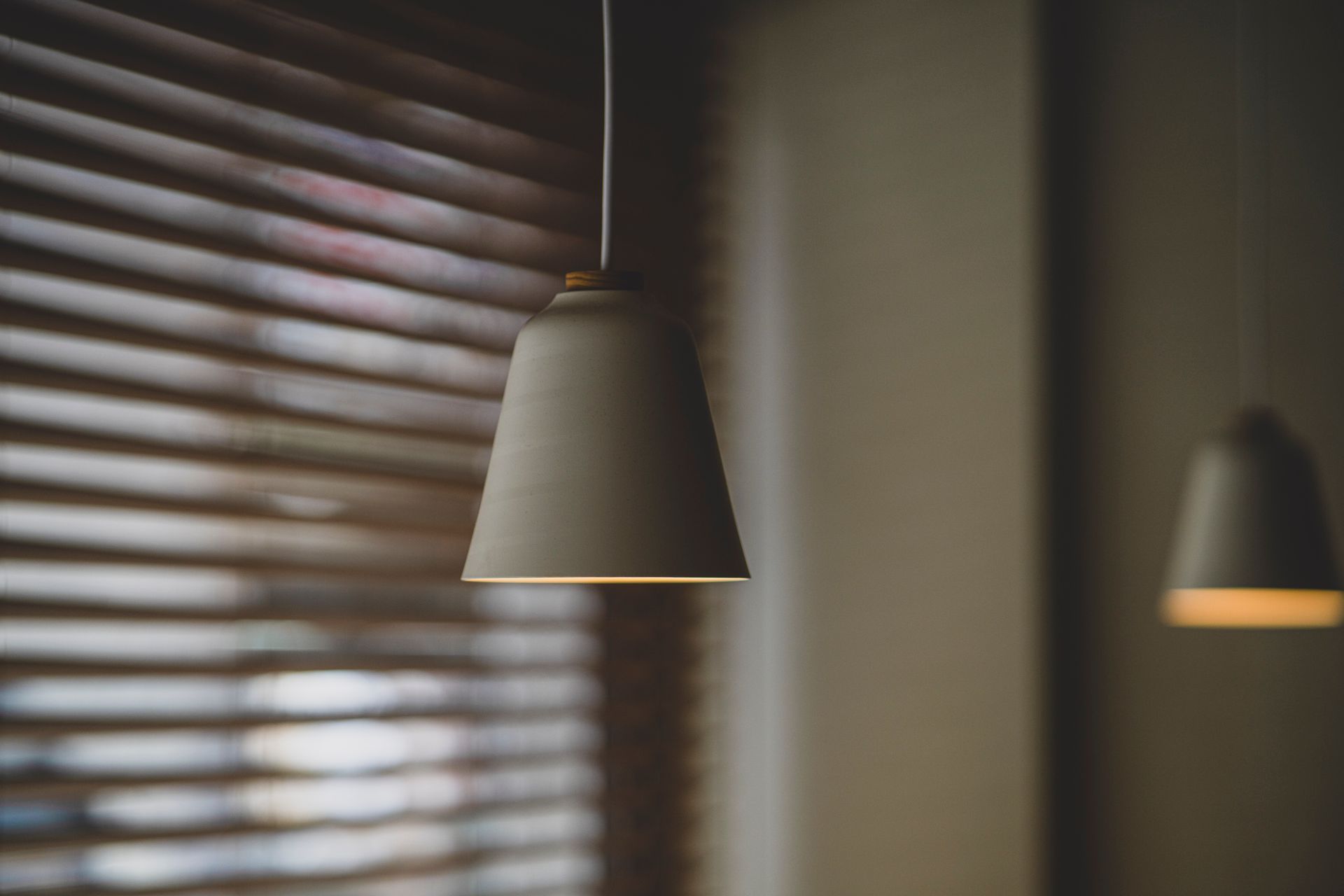 A minimalist pendant light against a soft focus background with window blinds.