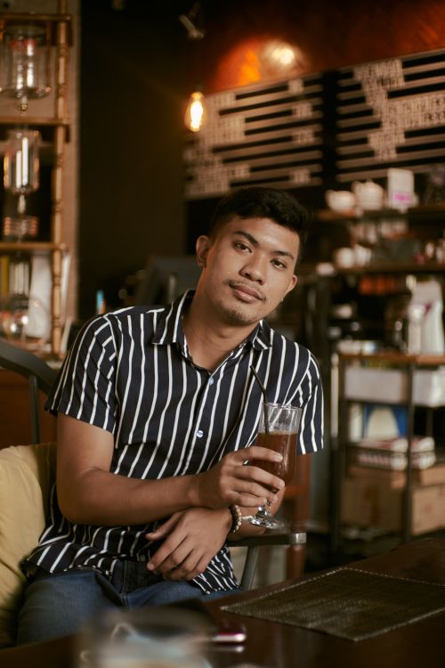 Free Young man enjoying a cool drink in a stylish coffee shop setting, relaxed atmosphere. Stock Photo