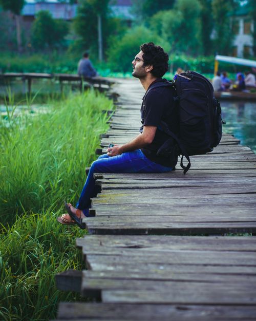 Free Adult man sitting on a wooden boardwalk by wetlands with a backpack, enjoying a peaceful moment. Stock Photo