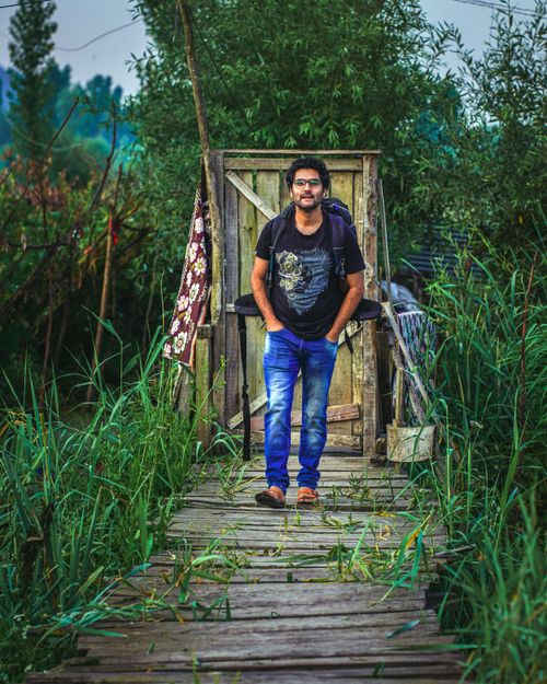 Free Man with eyeglasses and backpack walking on a wooden path through lush greenery. Stock Photo