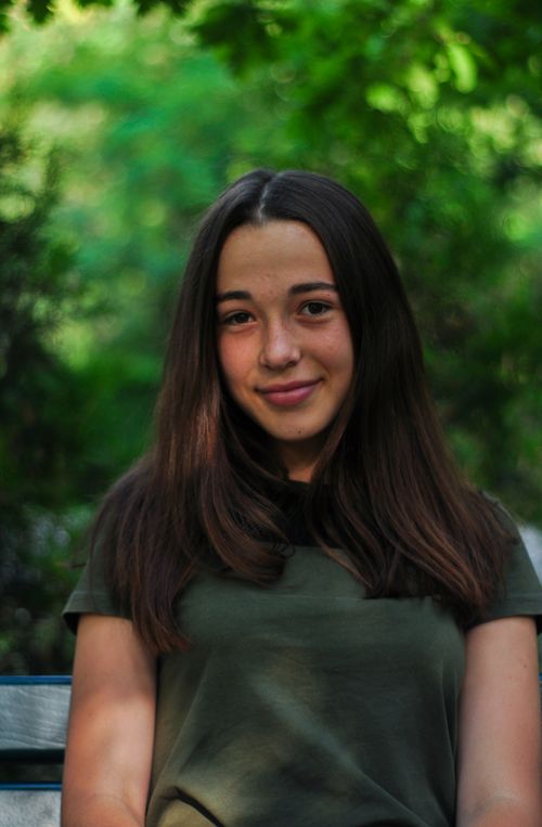Free Portrait of a teenage girl with long hair outdoors, surrounded by lush greenery. Stock Photo