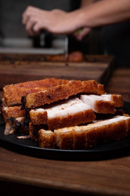 A sliced garlic herb pork loin roast fanned out on a wooden cutting board, showing a pink-blushed center and a browned herb crust, with pan sauce in a small dish alongside.