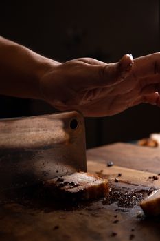A hand cutting roasted pork with a knife on a wooden board, shown in a dramatic close-up.