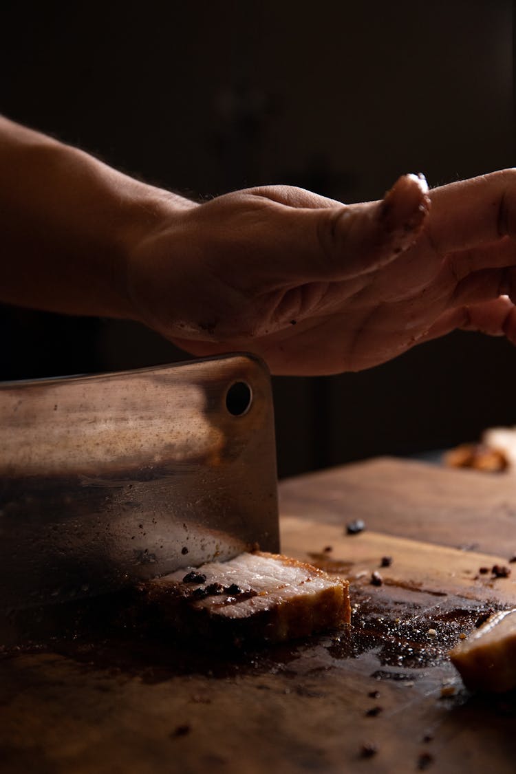 Close-up Of Person Cutting Meat With Knife