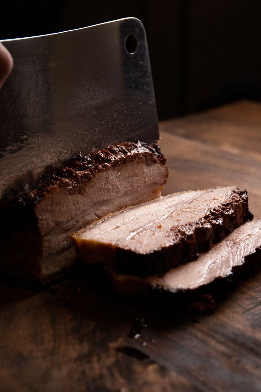 Thick slices of char-grilled pork shoulder with glossy dark molasses glaze, showing the pink interior and caramelized crust, served on a wooden cutting board