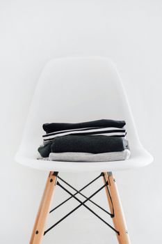A neatly folded stack of clothes on a white modern chair in a minimalist setting.