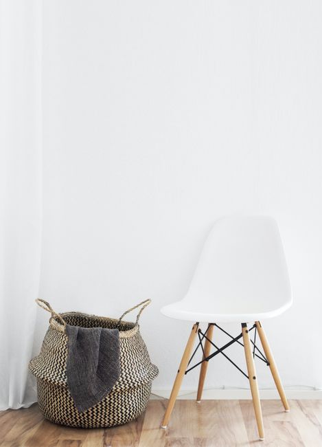 A minimalist interior featuring a white chair and a woven basket against a neutral background.