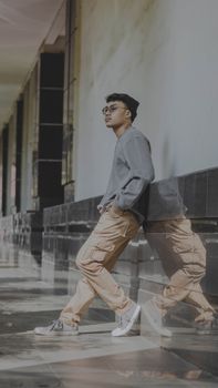 Stylish young man in a casual outfit leaning against a wall in a modern corridor.