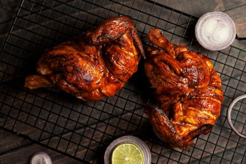 Free Juicy grilled chicken halves on a cooling rack, garnished with sliced lemon and red onions. Stock Photo