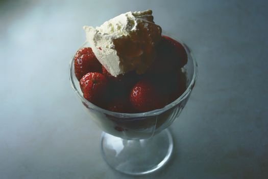 Close-up of fresh strawberries topped with rich cream in a glass, perfect for a sweet treat.
